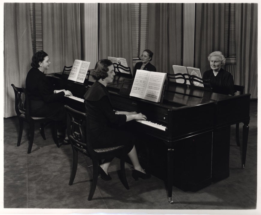 A photograph showing Dorothy playing the piano with three friends who are also playing piano.