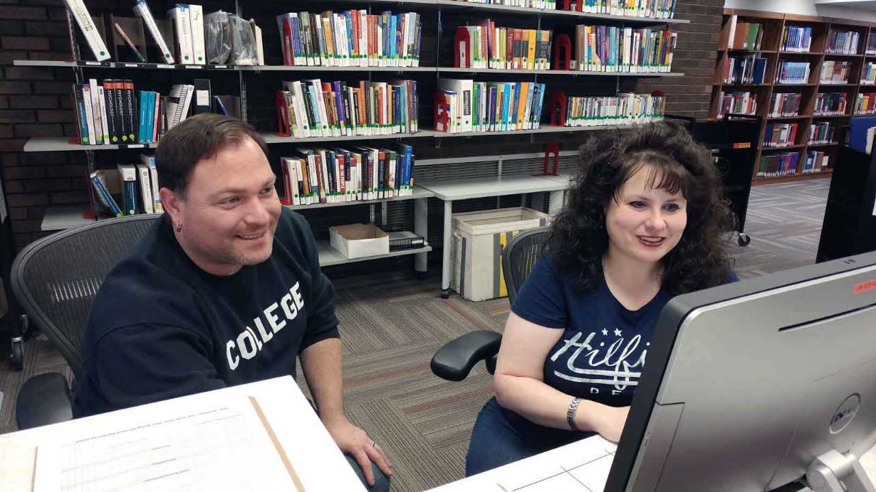 Student assistant and public services manager working together at a computer behind the information desk.