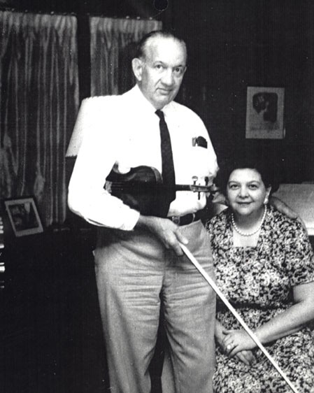 A photograph of Dorothy and Karl.  Dorothy is seated and Karl is holding a violin.